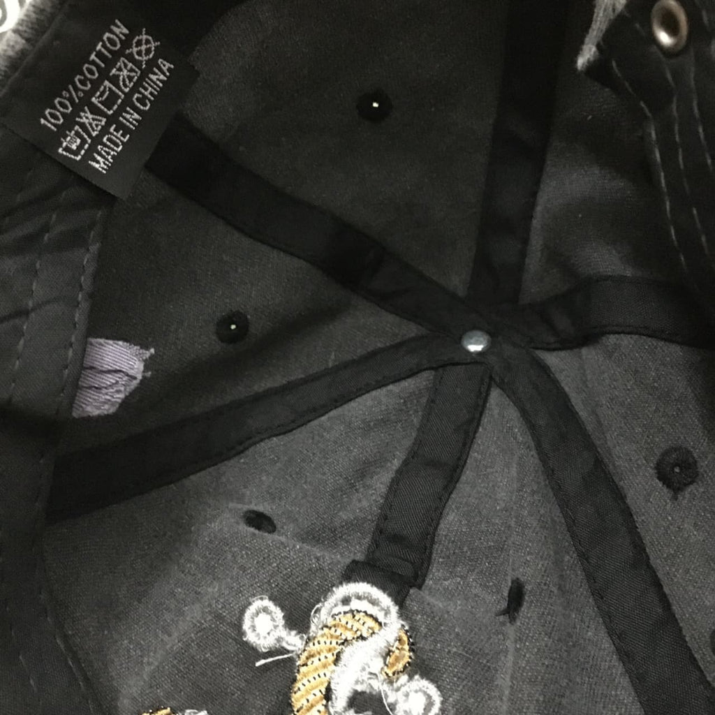 Close-up of the interior of a black baseball cap, showing the adjustable black fabric straps, metal snap closure, ventilation eyelets, and a small embroidered patch near the lower front.