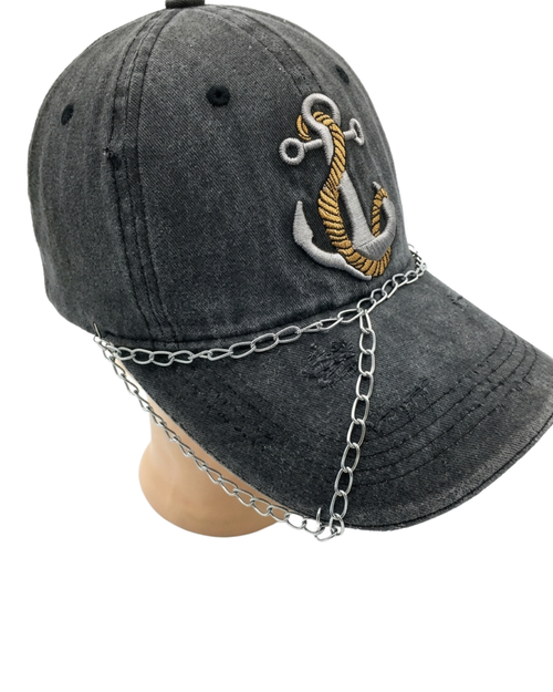 A dark gray washed baseball cap with an embroidered anchor on the front, featuring a silver metal chain draped over the brim and down the side, displayed on a mannequin head against a white background.