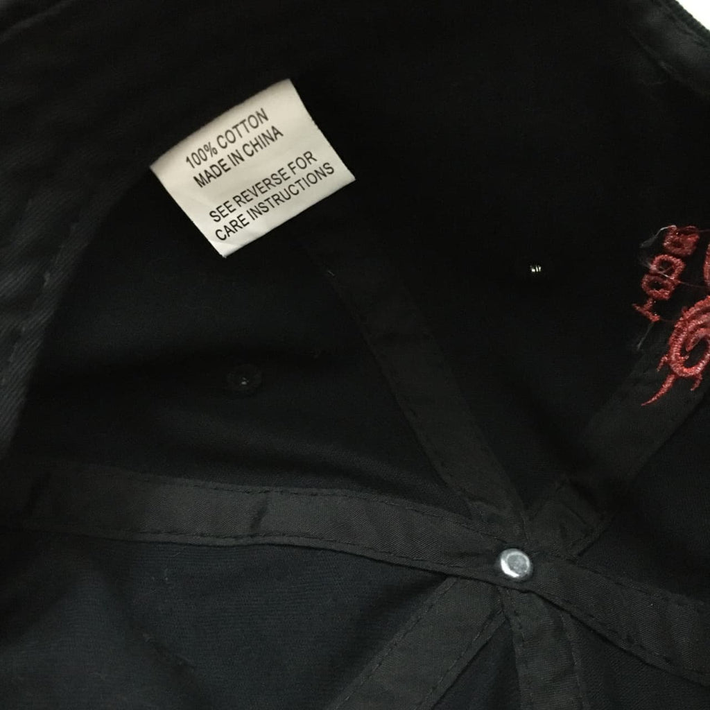 Close-up of a black cotton garment interior showing a sewn-in care label that reads '100% COTTON MADE IN CHINA SEE REVERSE FOR CARE INSTRUCTIONS' and a small red embroidered logo on the side.