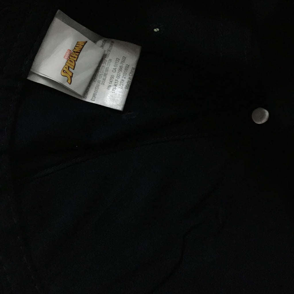Close-up of a black garment with a visible white Marvel Spider-Man size tag and a silver snap button.