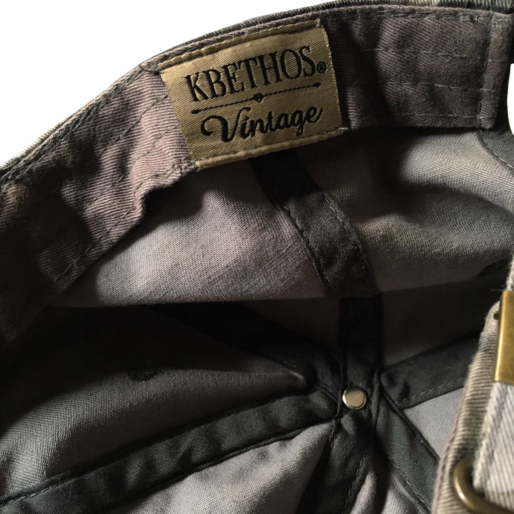 Close-up of the interior of a vintage Kbethos cap, showing the inner crown, a tan Kbethos Vintage label stitched onto the inside of the crown, and a brass button closure.